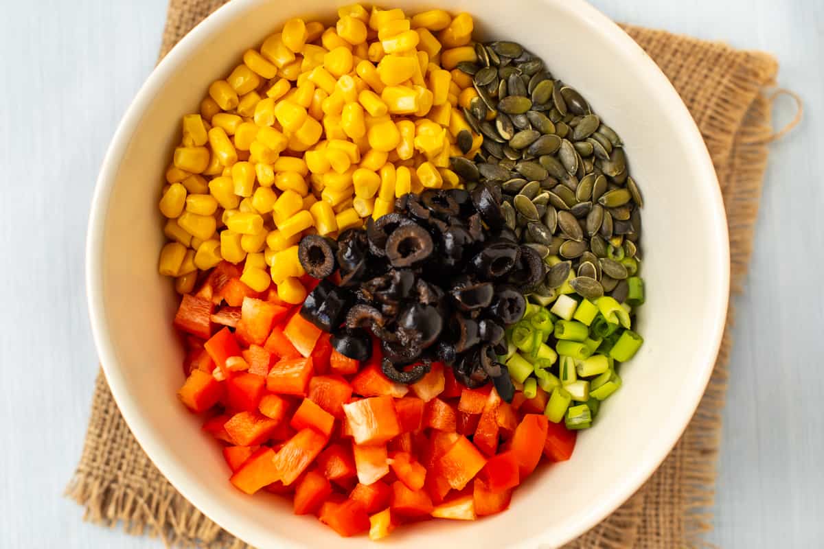 Fresh vegetables and black olives in a mixing bowl.