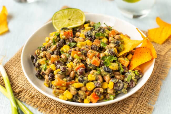 A bowlful of creamy bean salad with fresh lime and tortilla chips on the side.