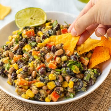 A hand scooping creamy cowboy caviar with a tortilla chip.