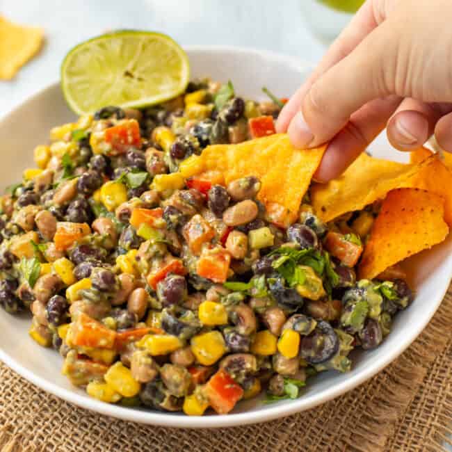 A hand scooping creamy cowboy caviar with a tortilla chip.