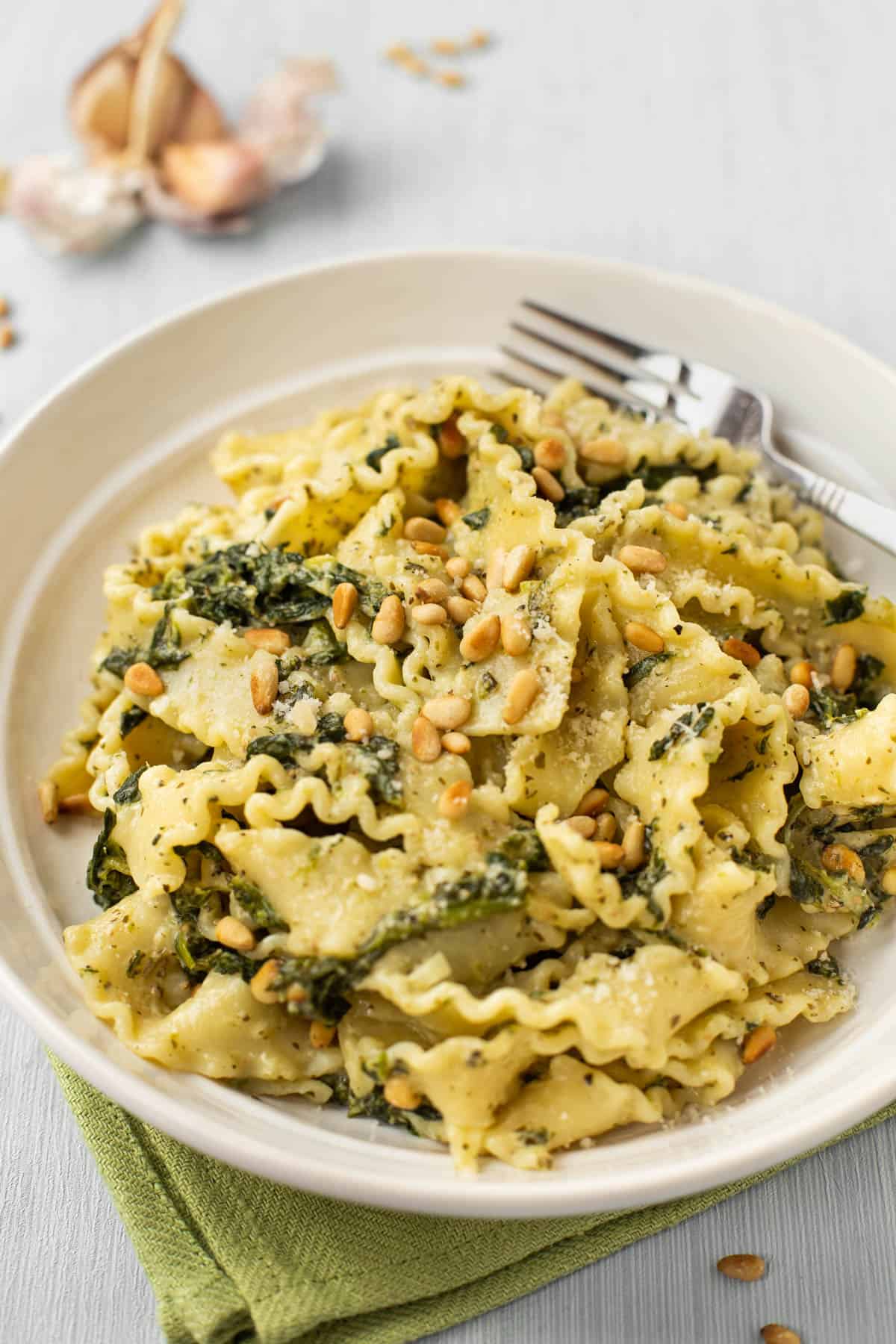 A bowl of mafalde pasta with creamy spinach sauce and pine nuts.
