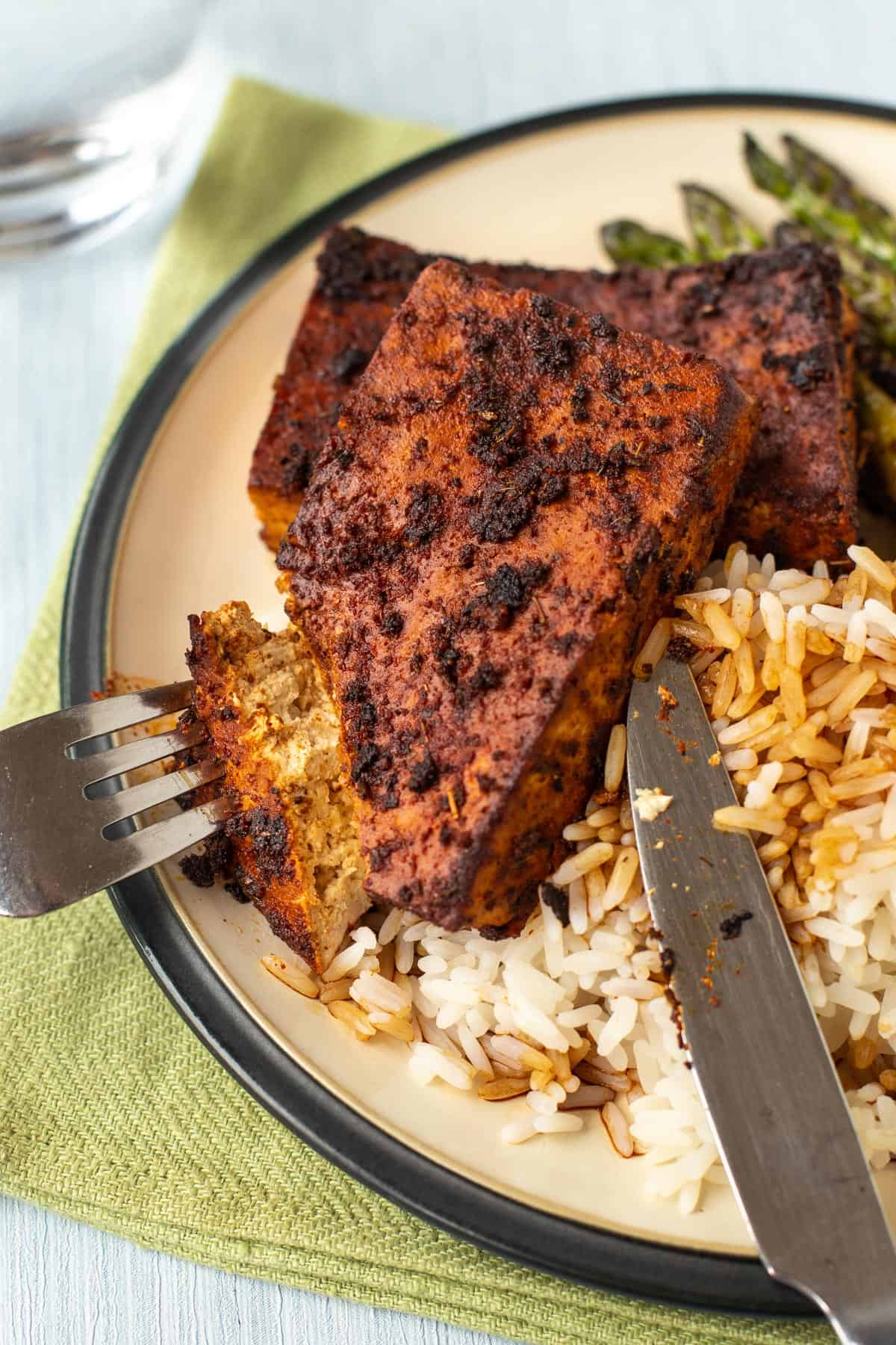 A blackened tofu steak being cut open, served with rice.