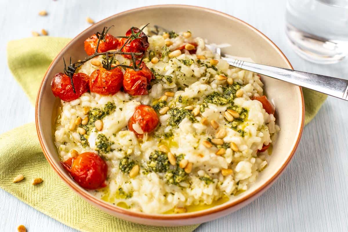A portion of cheesy tomato risotto topped with pesto and pine nuts.