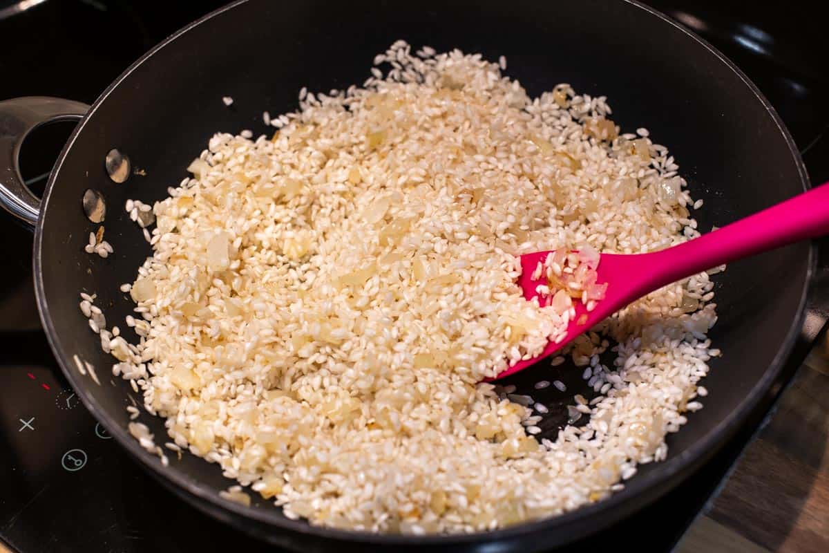 Uncooked risotto rice in a wok with onion and garlic.