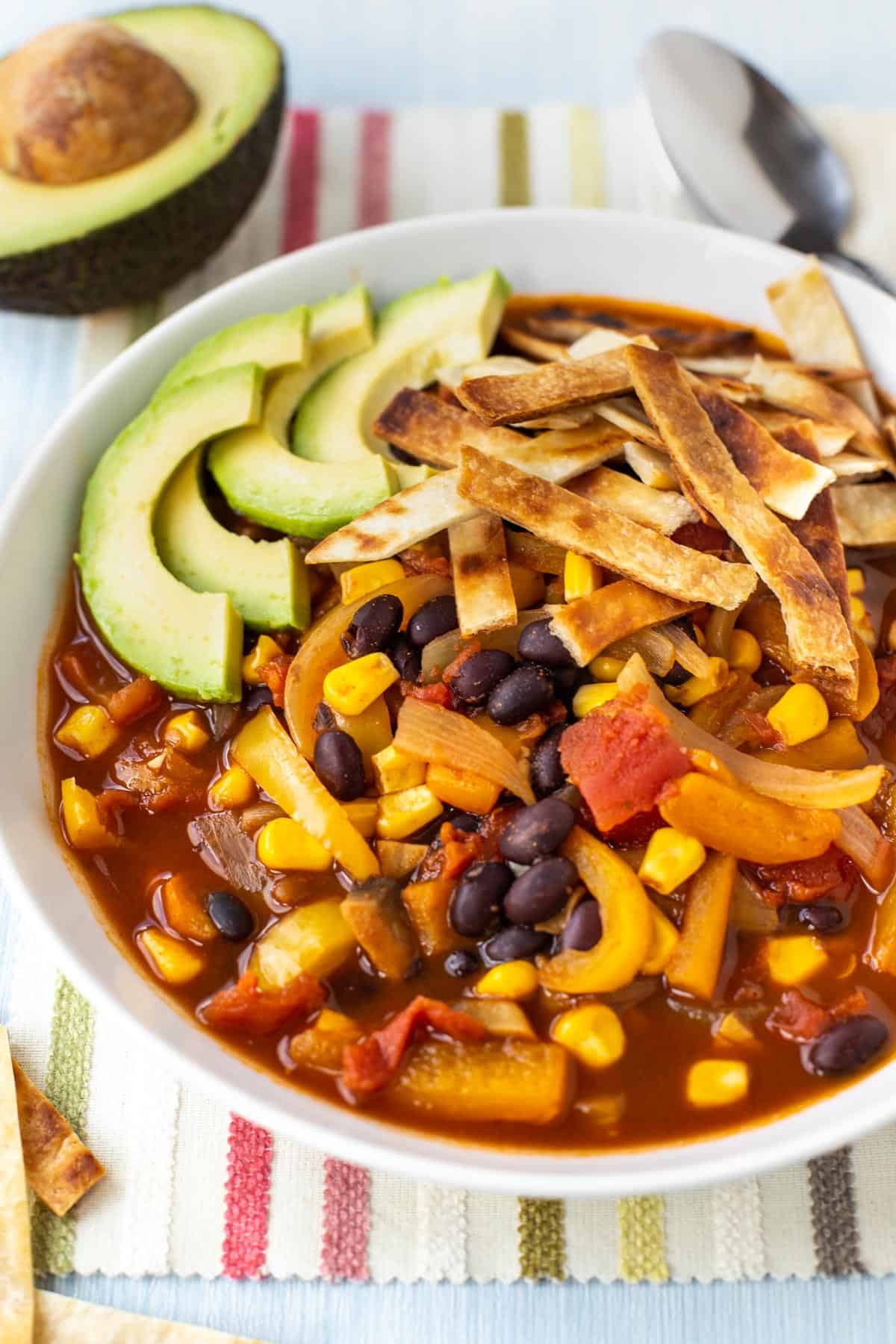 Vegan taco soup in a bowl topped with avocado and tortilla strips.
