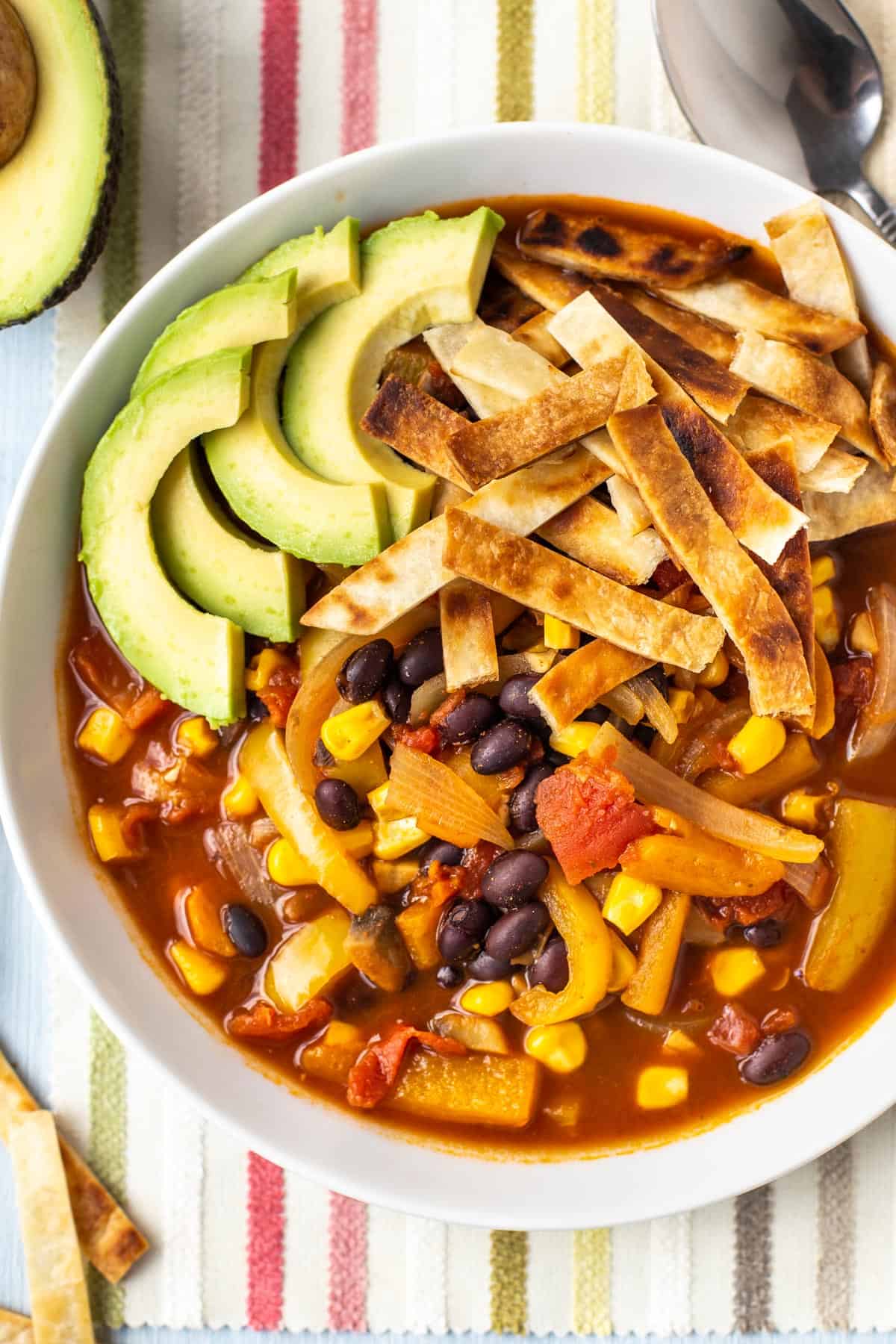 Vegan taco soup topped with sliced avocado and crispy tortilla strips.