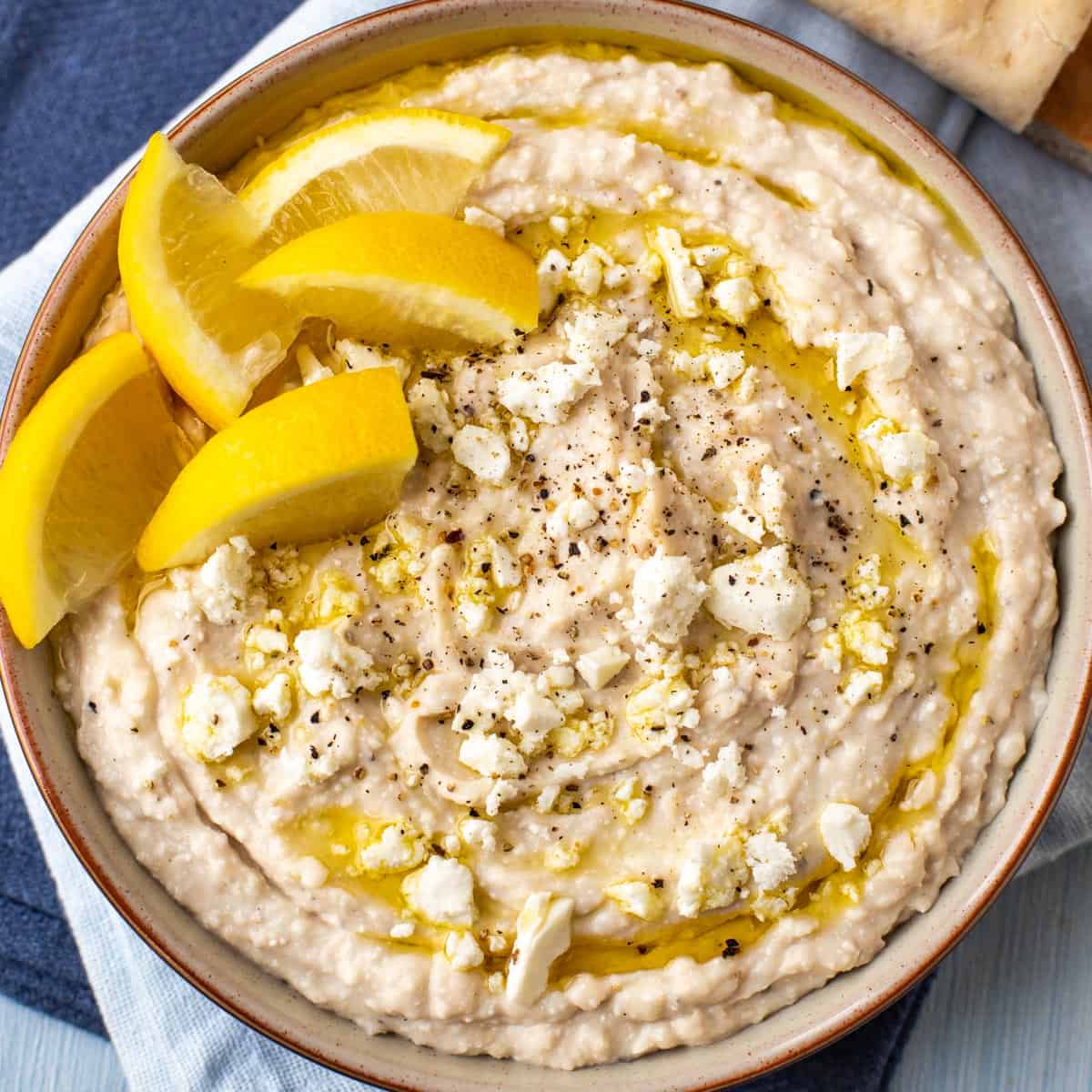 White bean hummus topped with lemon wedges and crumbled feta cheese.