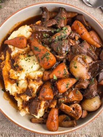 A bowlful of rich mushroom bourguignon stew served over mashed potato.