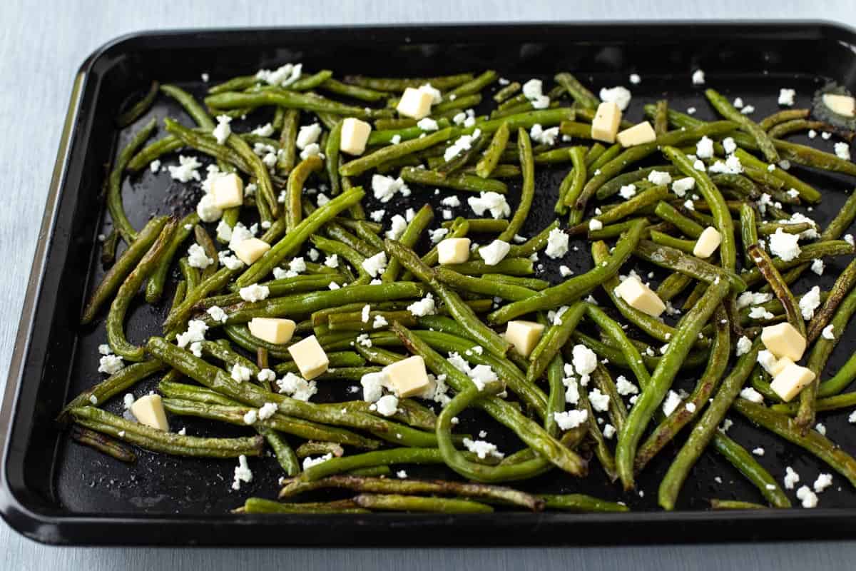 Roasted green beans are scattered with cubes of butter and feta cheese.