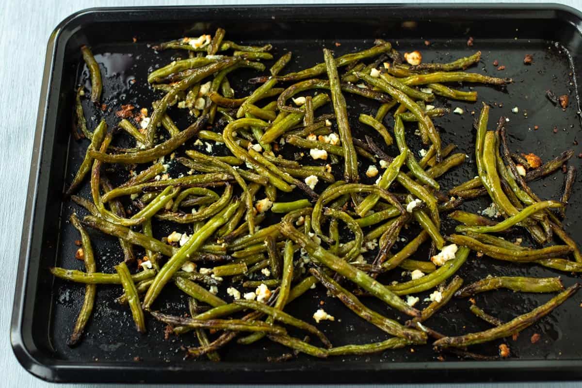 Crispy roasted green beans on a baking tray with feta cheese.