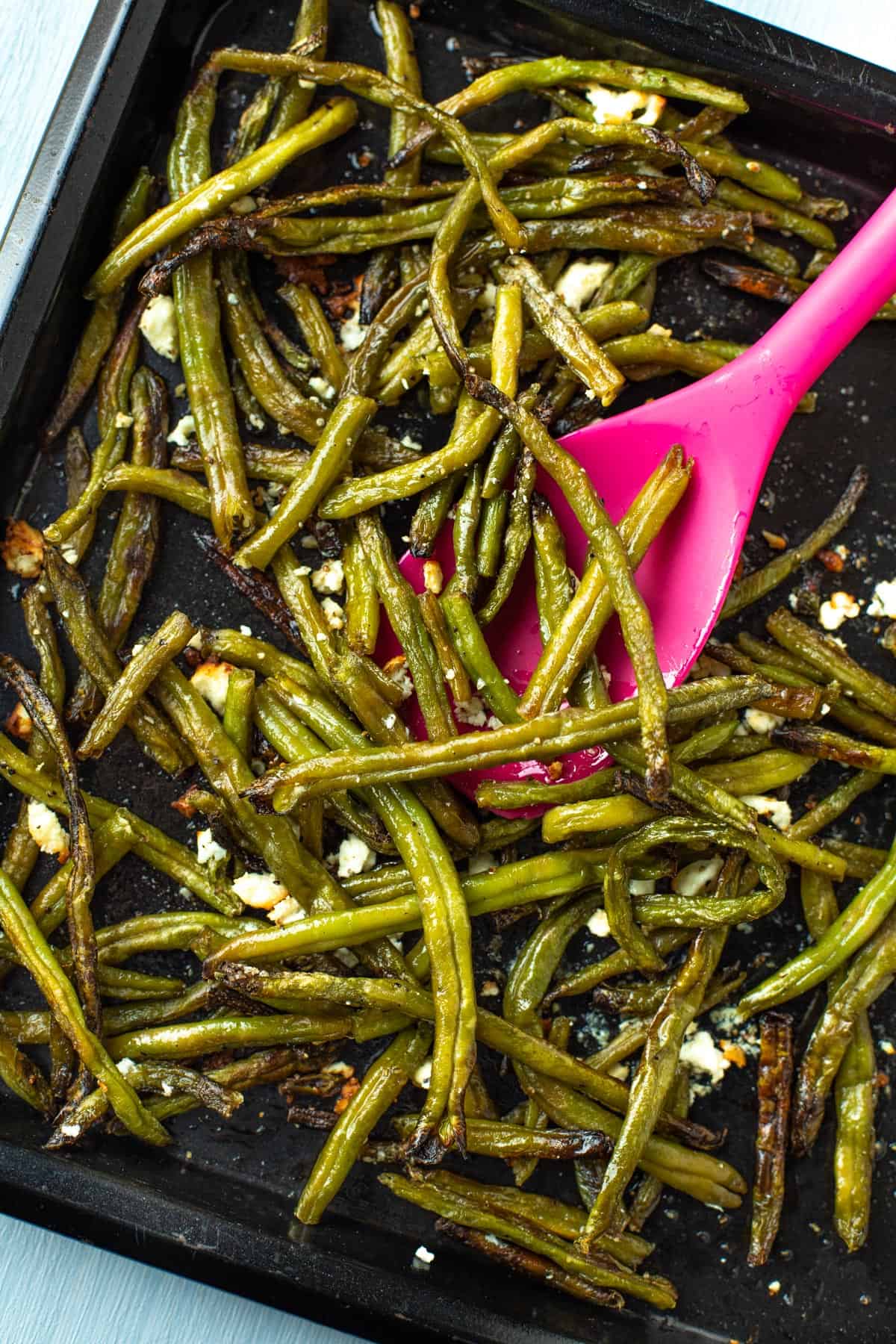 Roasted green beans with feta and lemon juice on a baking tray.