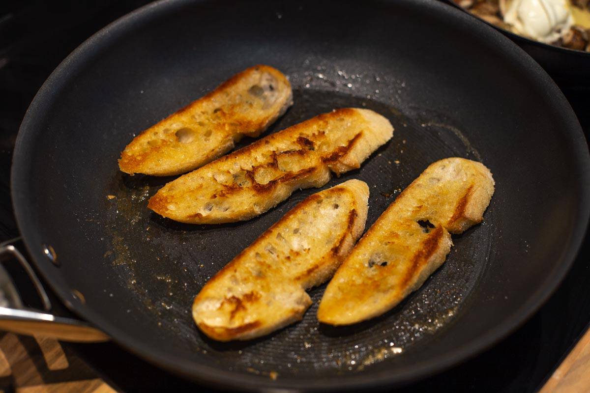 Slices of baguette crisping up in a frying pan.