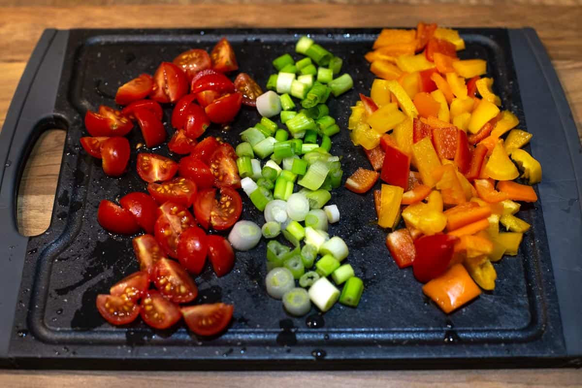 Chopped cherry tomatoes, spring onions and peppers on a cutting board.
