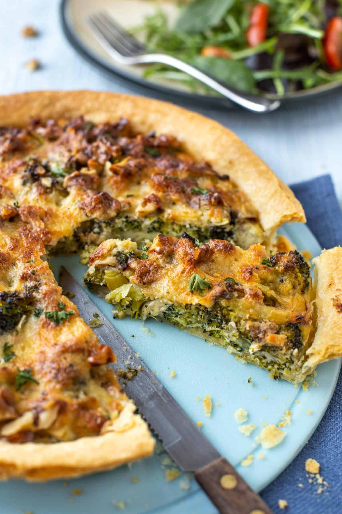 A slice being cut from a cheese and broccoli tart.