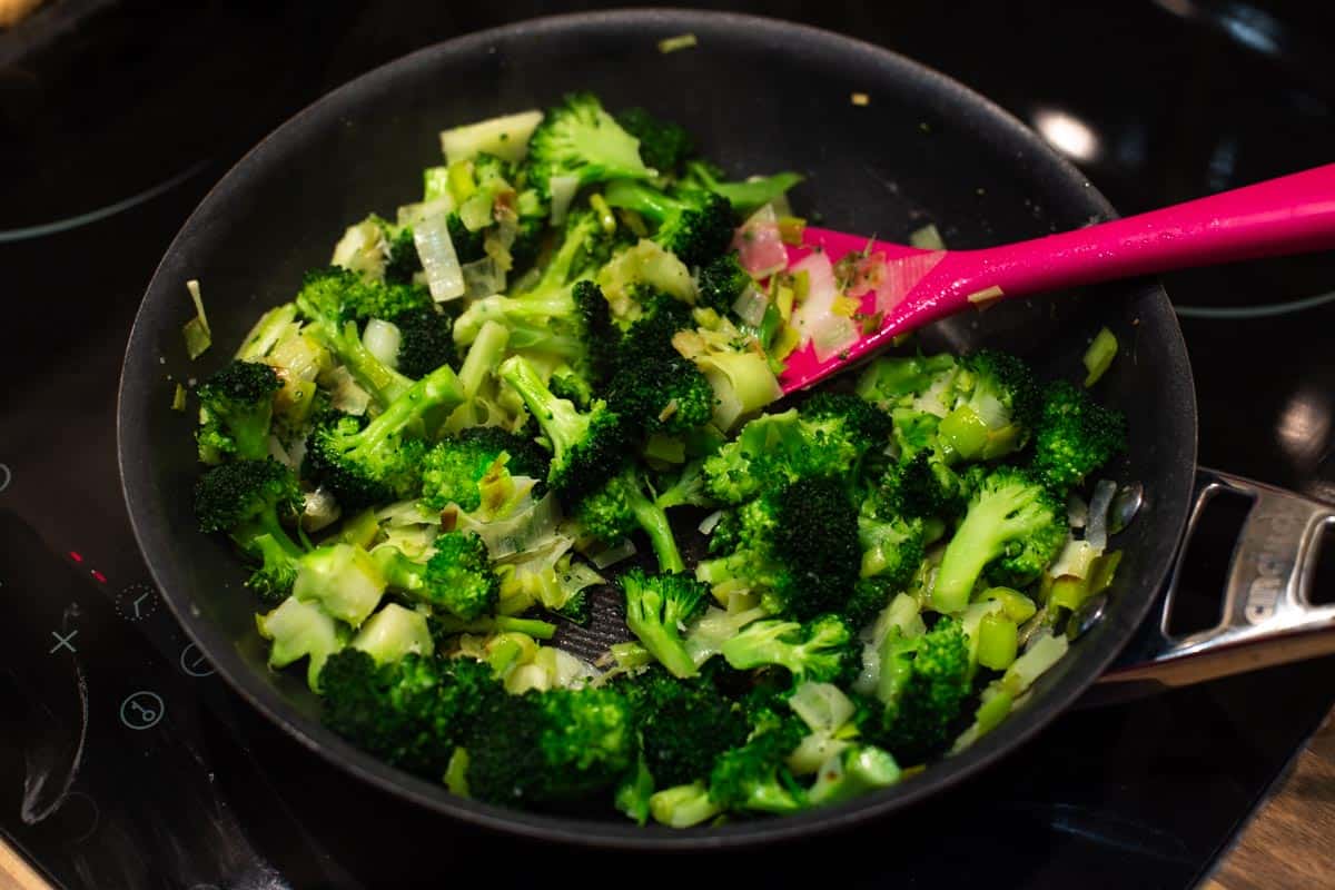 Broccoli and leeks cooking in a frying pan.