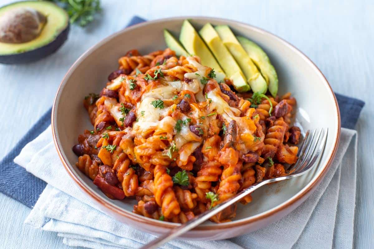 Vegetarian chilli mac in a bowl with sliced avocado.