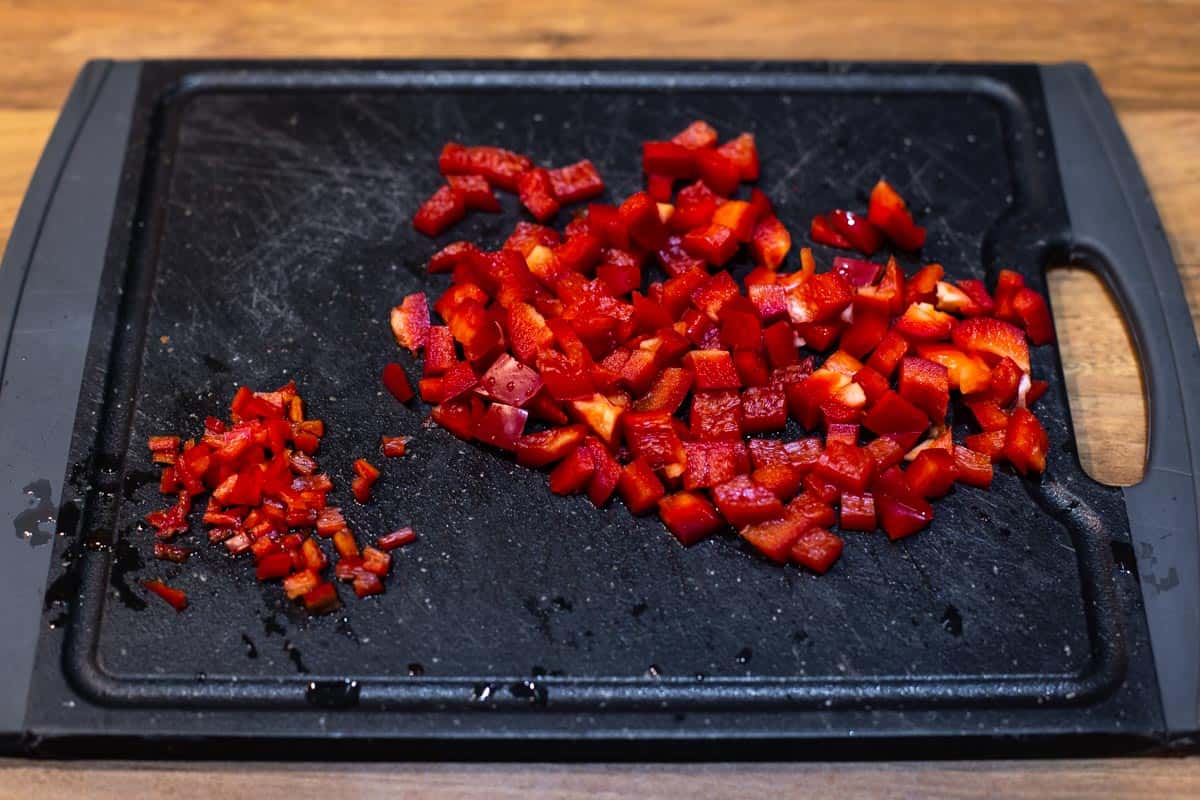 Diced red chilli and red bell pepper on a chopping board.