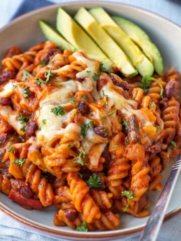 Cheesy vegetarian chilli mac in a bowl with sliced avocado.