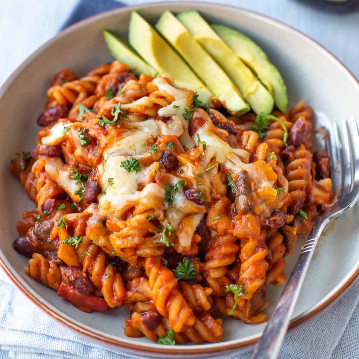 Cheesy vegetarian chilli mac in a bowl with sliced avocado.