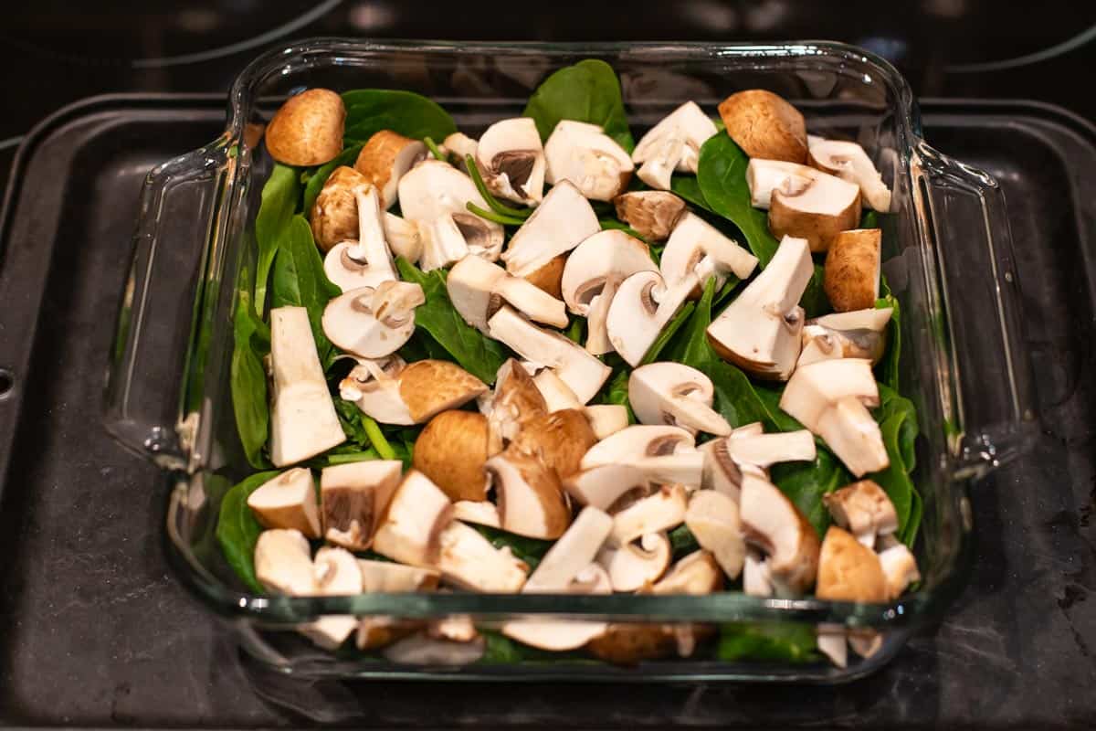 Raw spinach and mushrooms in a baking dish.