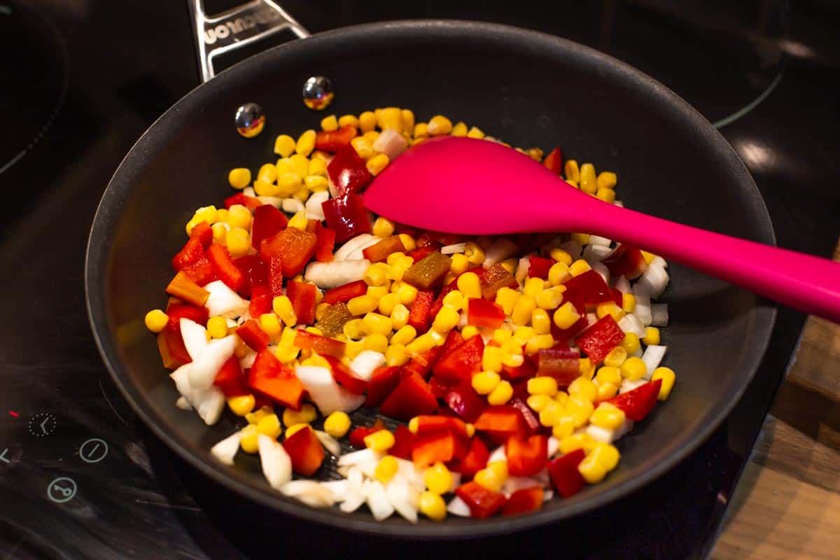 Sweetcorn, pepper and onion cooking in a frying pan.
