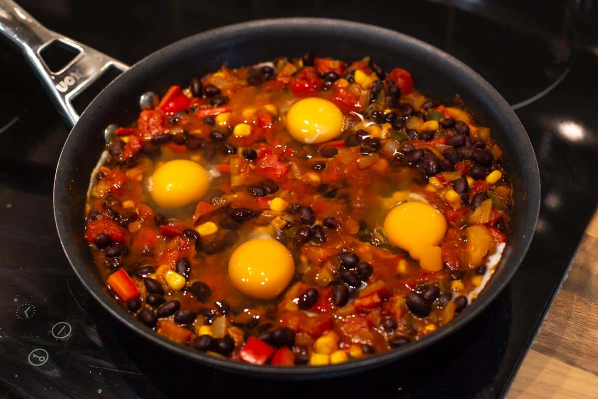 Eggs cracked on top of bean chilli in a pan.