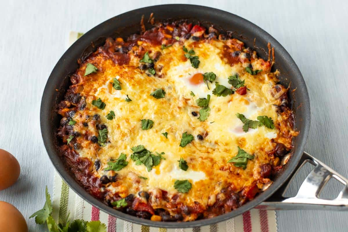 Mexican baked eggs in a frying pan, topped with melted cheese.