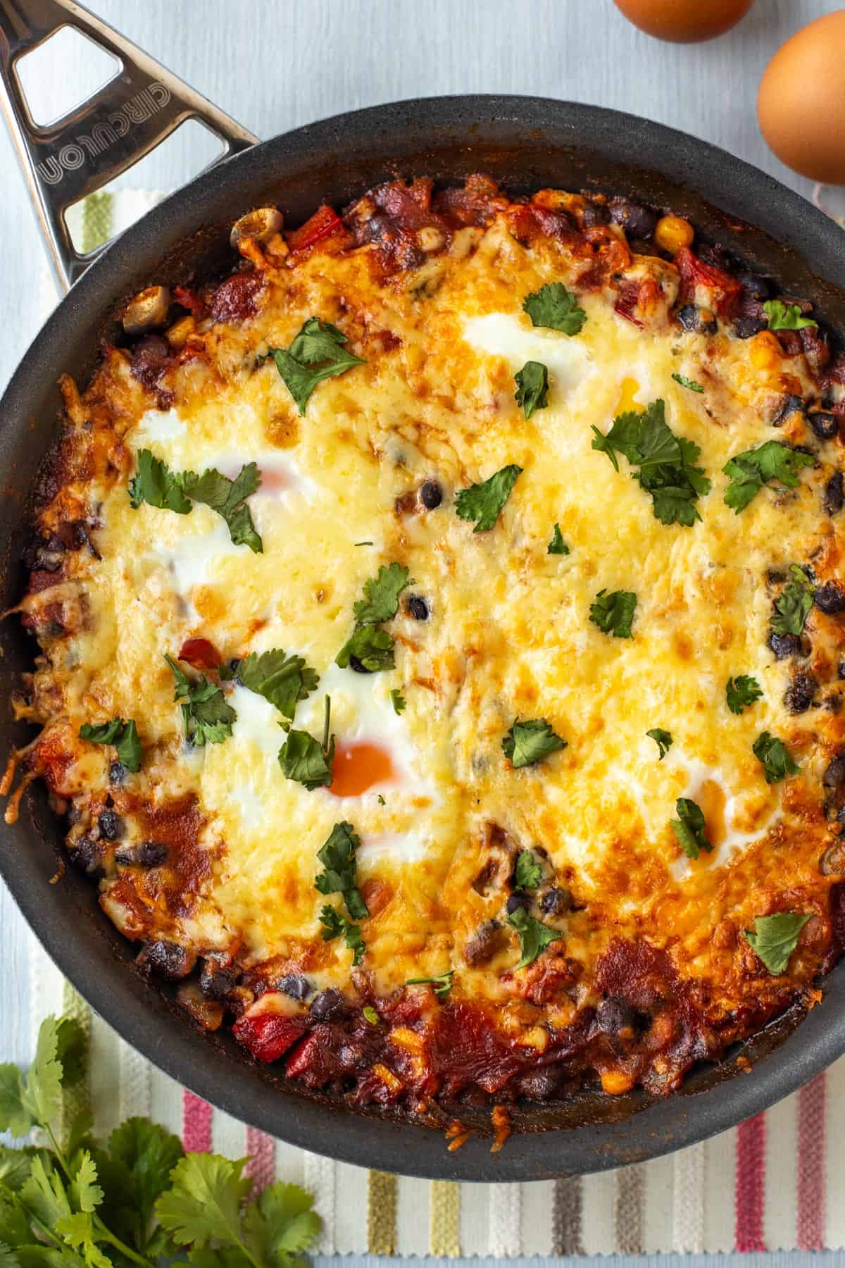 Mexican baked eggs in a frying pan, topped with melted cheese and cilantro.