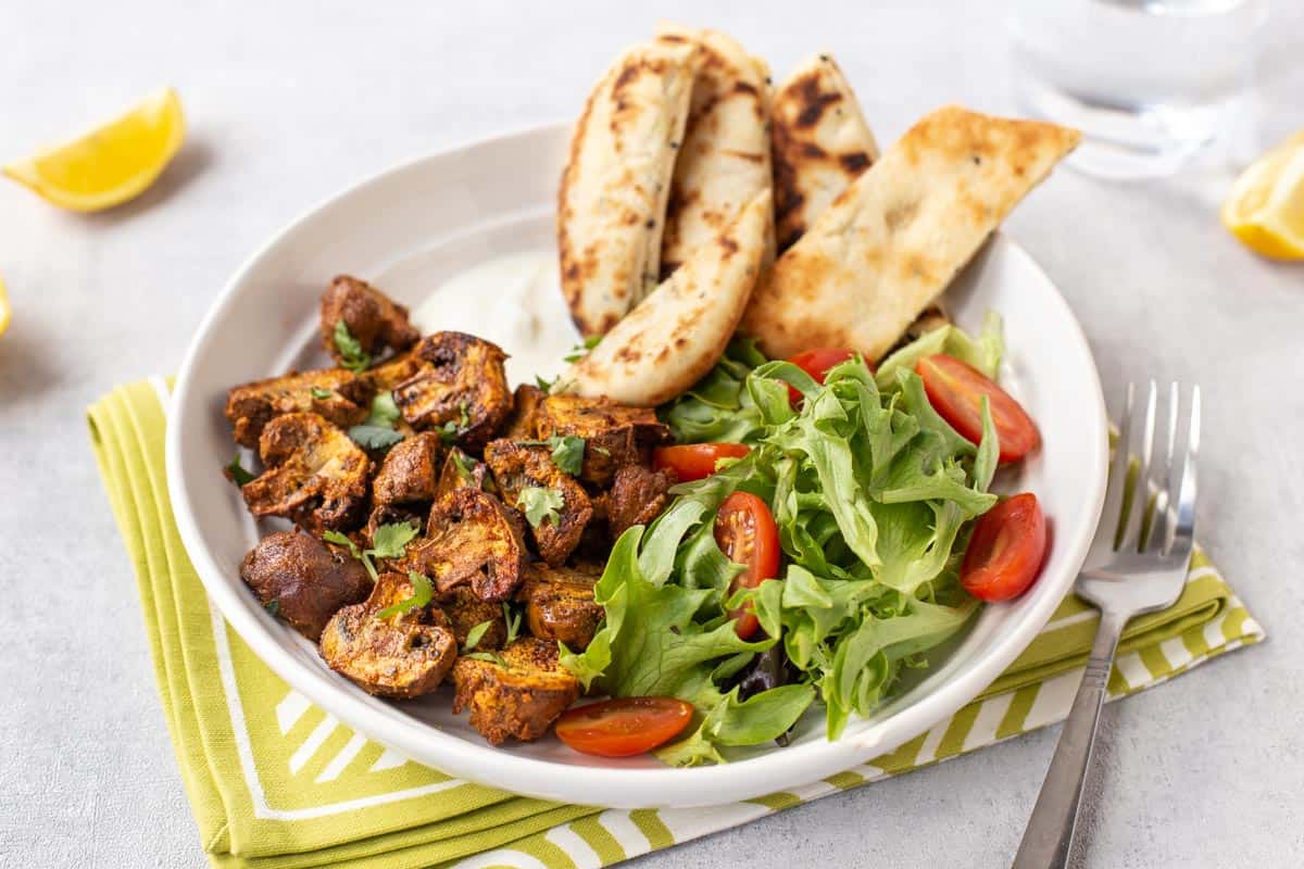 Baked mushroom tikka in a bowl with salad and naan bread.