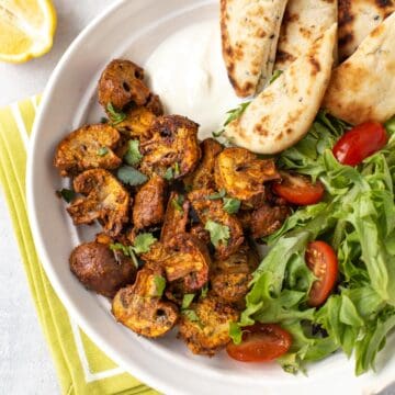 Baked mushroom tikka in a bowl with naan bread and salad.