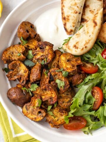 Baked mushroom tikka in a bowl with naan bread and salad.