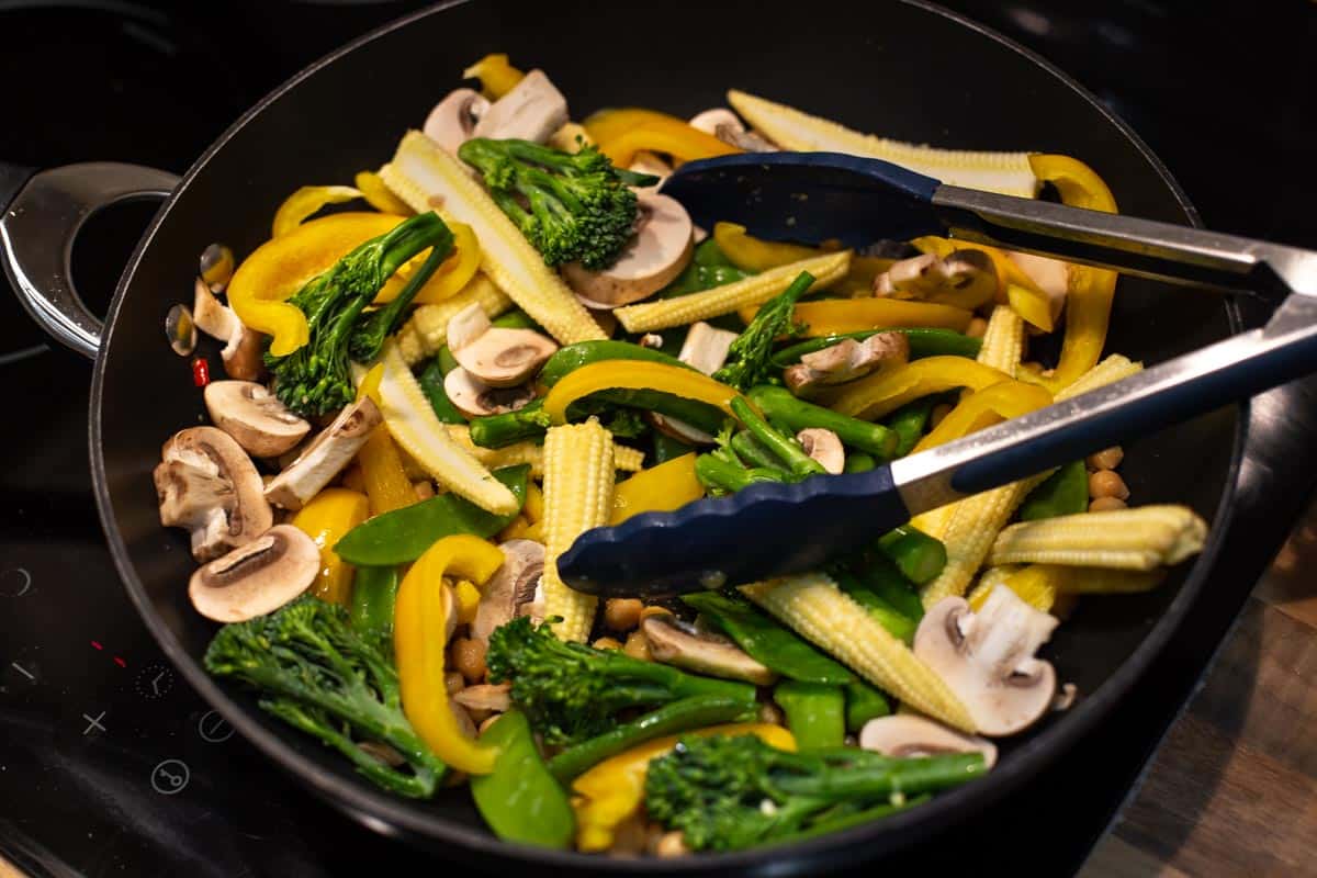 Stir fry vegetables cooking in a wok with a pair of tongs.