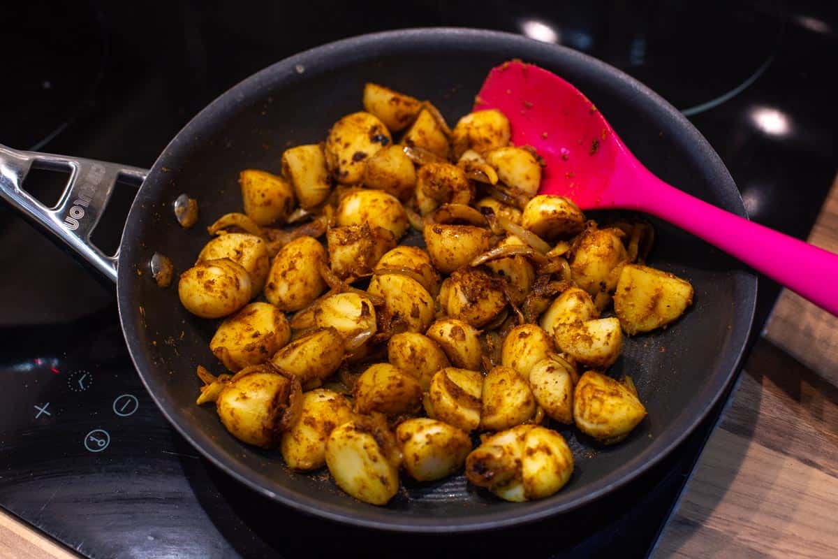 Tinned potatoes being cooked in a frying pan with onions and spices.