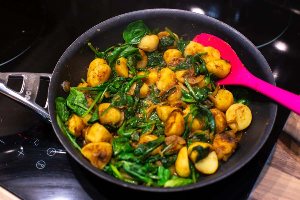Spinach and potato curry cooking in a frying pan.