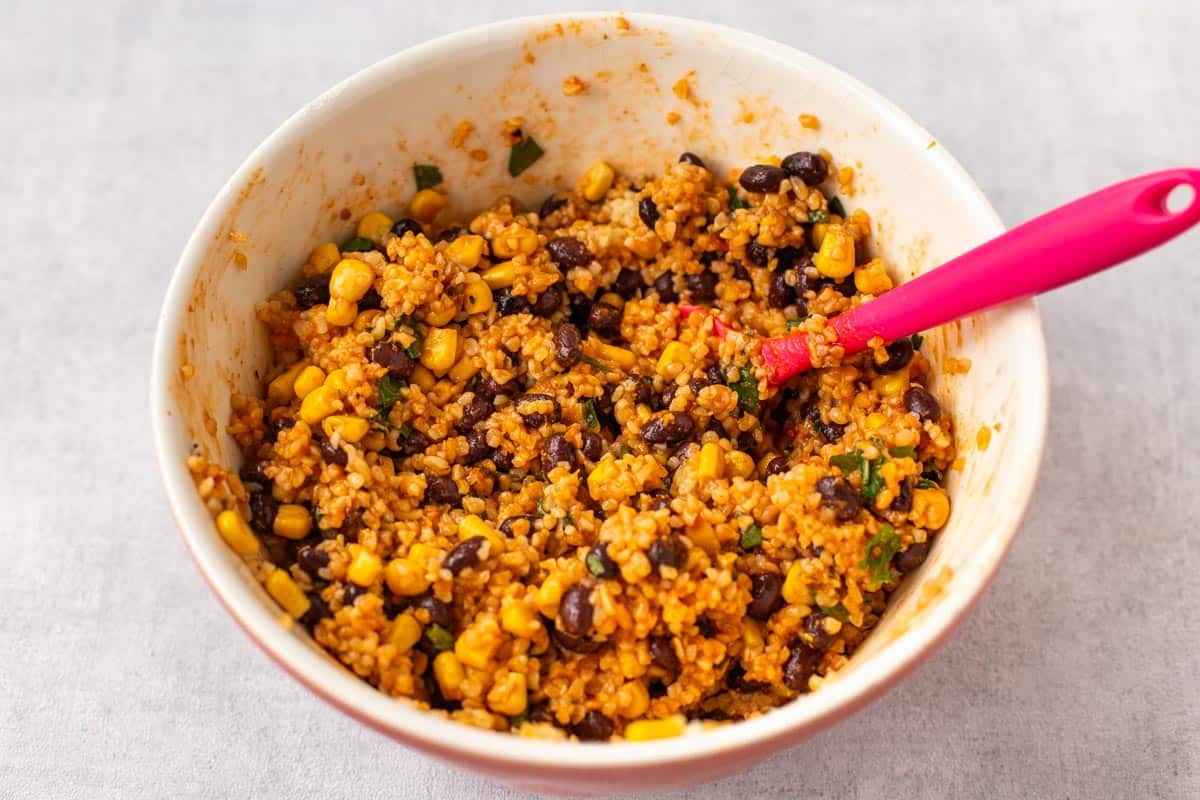Bulgur wheat mixed with black beans, corn and pesto in a mixing bowl.