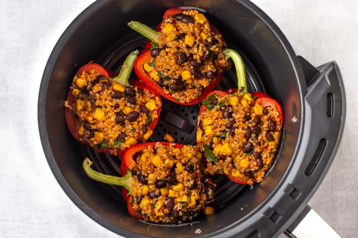 Red peppers stuffed with bulgur wheat and black beans, in an air fryer basket.