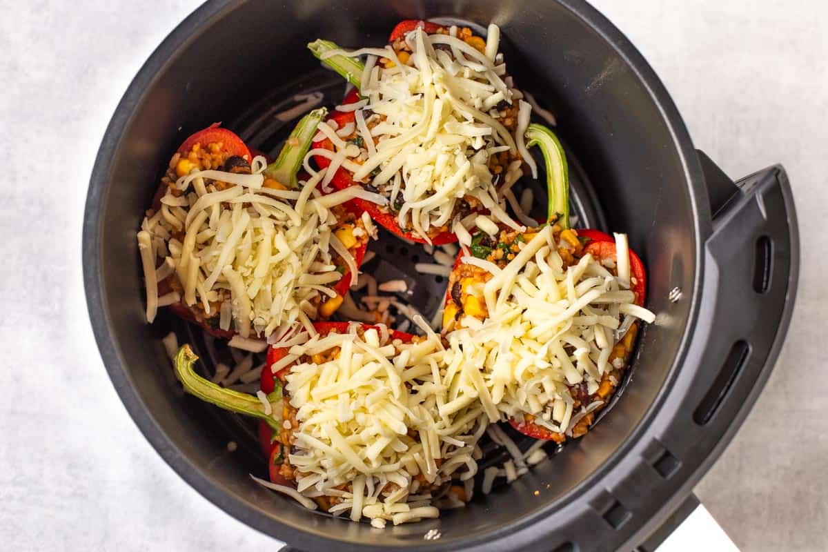 Stuffed peppers topped with grated cheese in an air fryer basket.