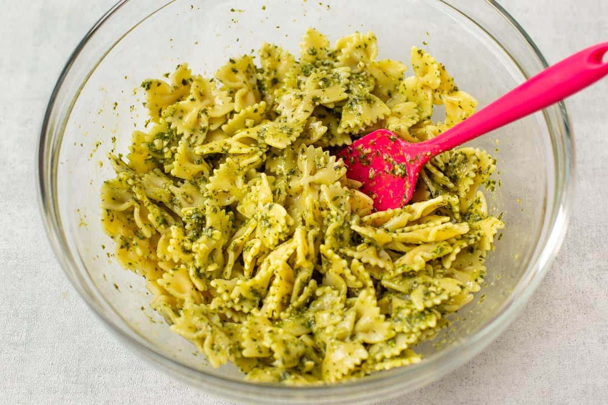 Farfalle pasta coated with basil pesto in a mixing bowl.
