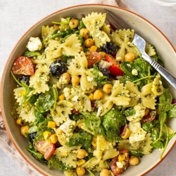 A bowlful of chickpea pasta salad with black olives and arugula.
