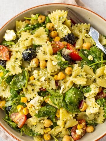 A bowlful of chickpea pasta salad with black olives and arugula.