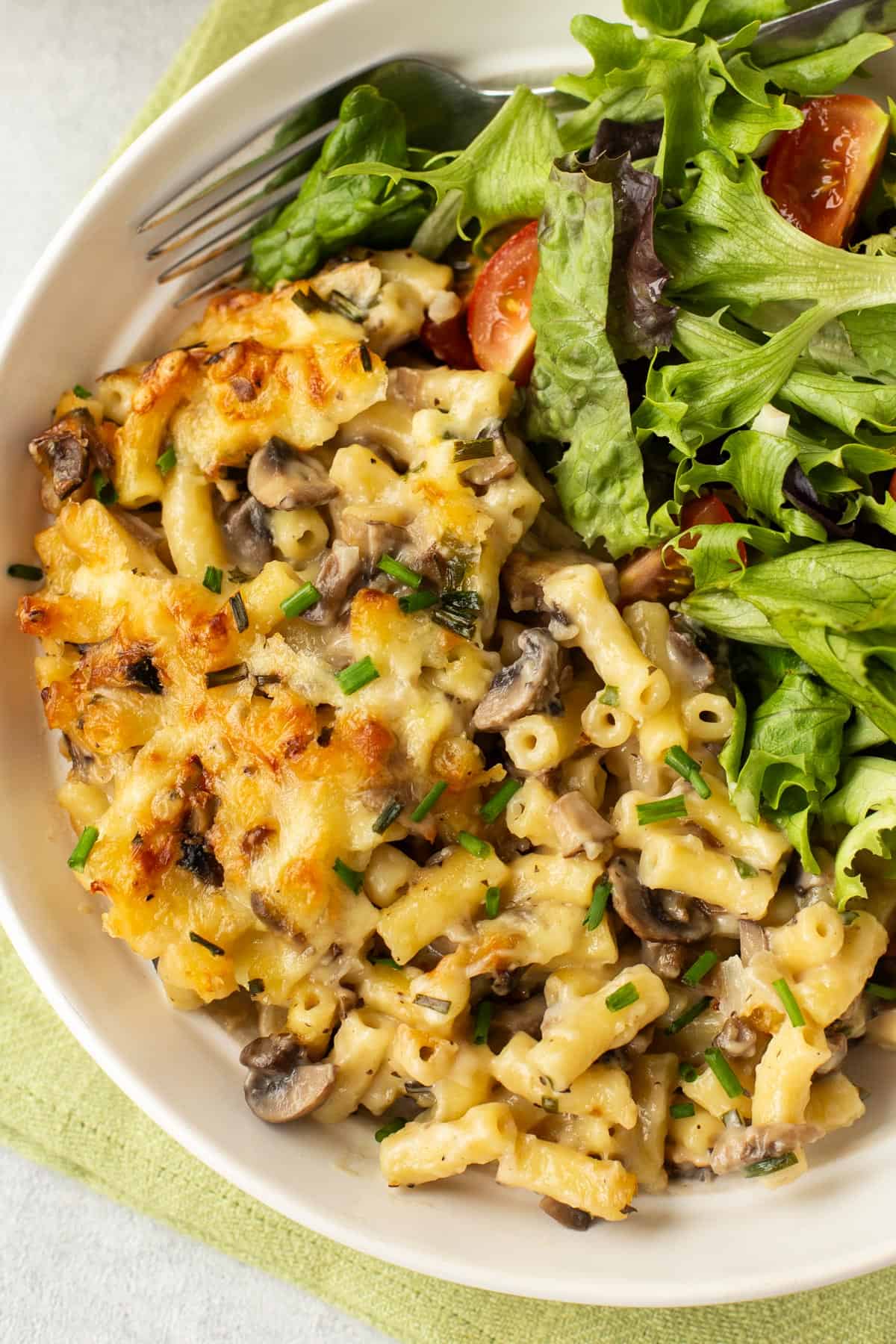 A portion of garlic mushroom mac and cheese in a bowl with salad.