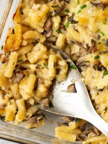 Garlic mushroom mac and cheese being scooped by a large spoon.