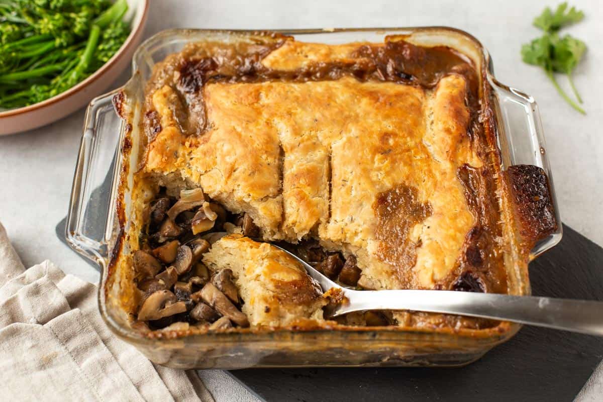 Mushroom pie with a suet topping being scooped from a baking dish with a large spoon.