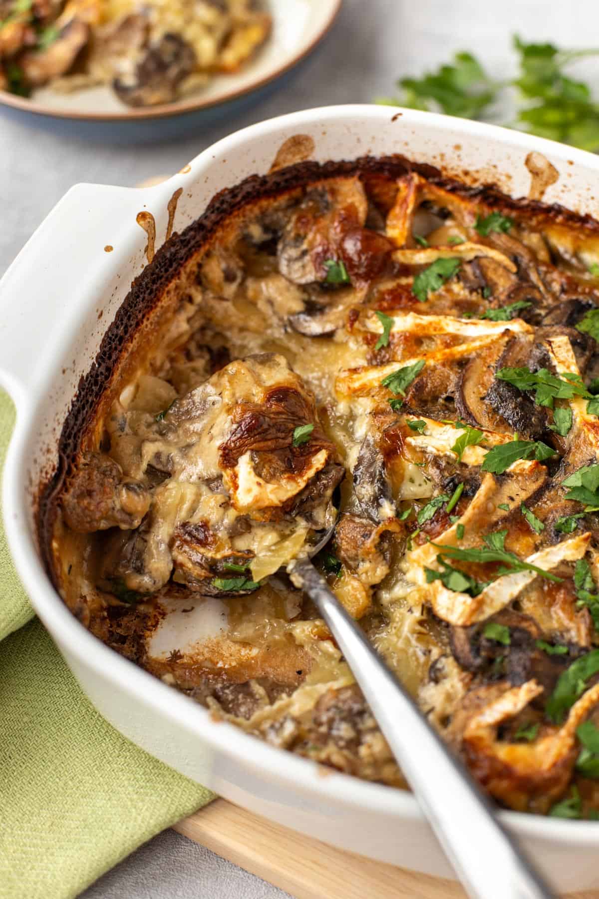Creamy potato and mushroom gratin with brie in a baking dish, with a scoop removed.