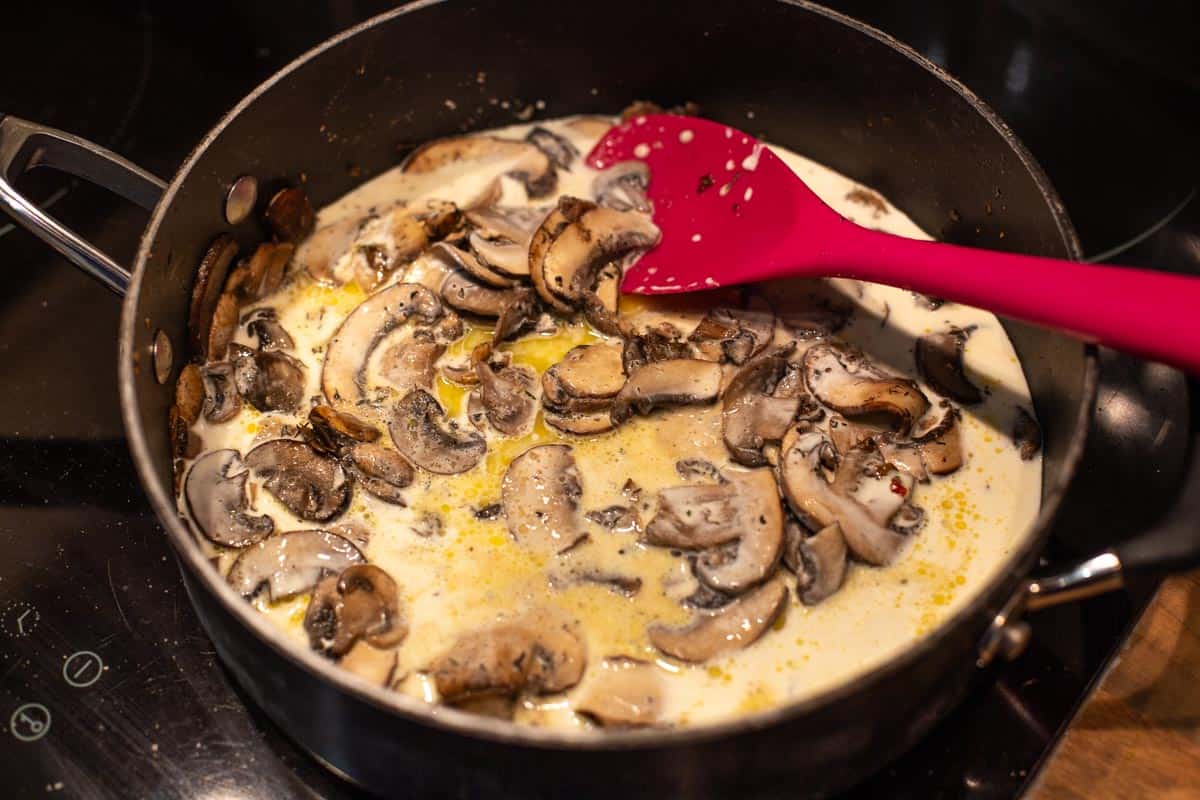Sliced mushrooms cooking in a frying pan in a cream sauce.