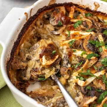 Creamy mushroom and potato gratin in a dish being scooped with a spoon.
