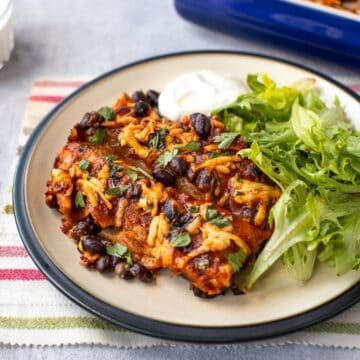 Vegetarian enchiladas on a plate with black beans and sour cream.