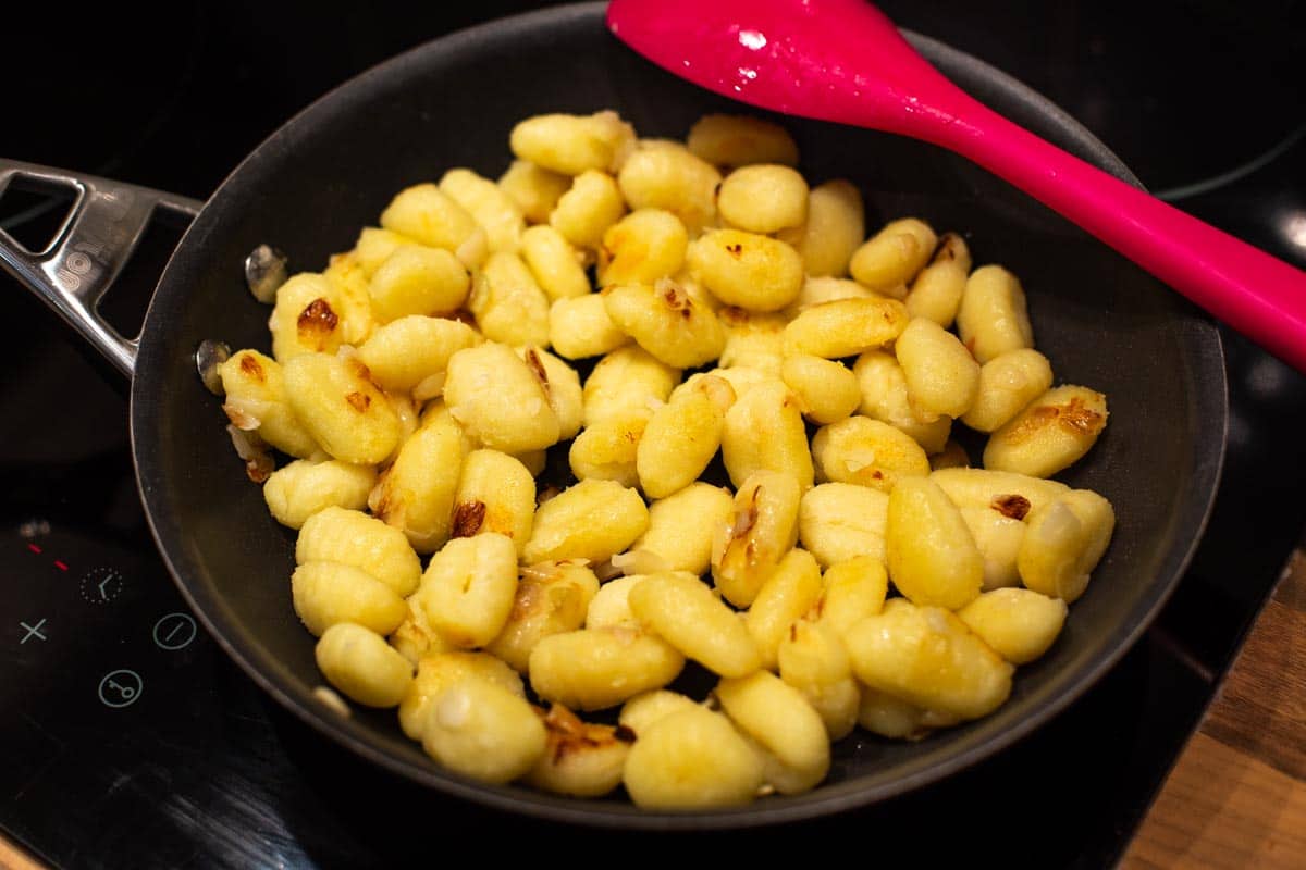 Fried gnocchi cooking in a frying pan.