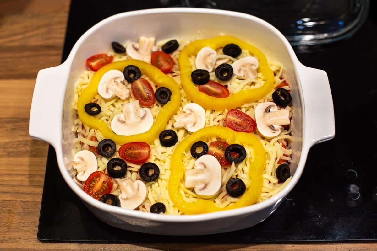 A baking dish with mozzarella and vegetable pizza toppings.