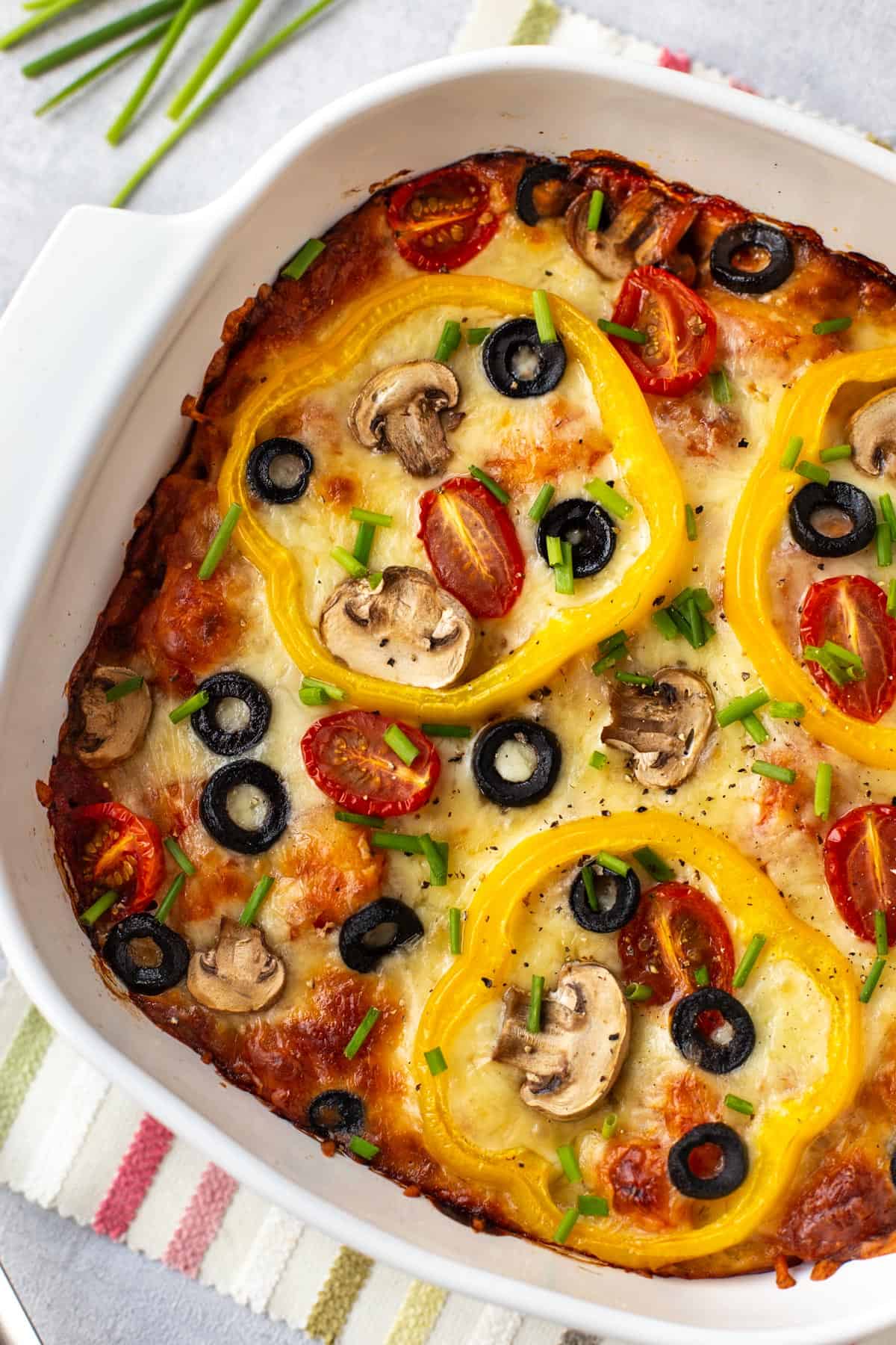 Gooey pizza baked gnocchi in a dish, topped with peppers, mushrooms and olives.